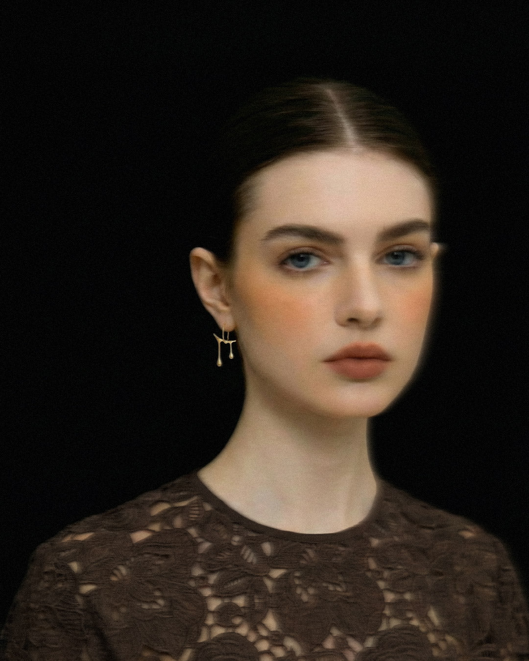 Woman wearing Chopin gold earrings against a black background