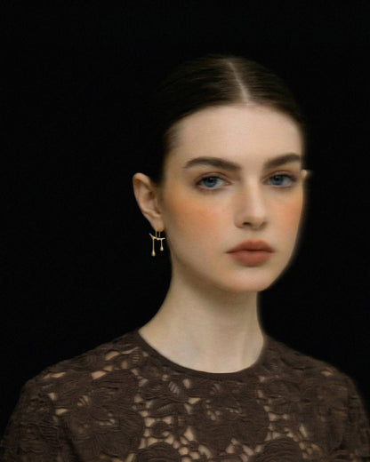 Woman wearing Chopin gold earrings against a black background