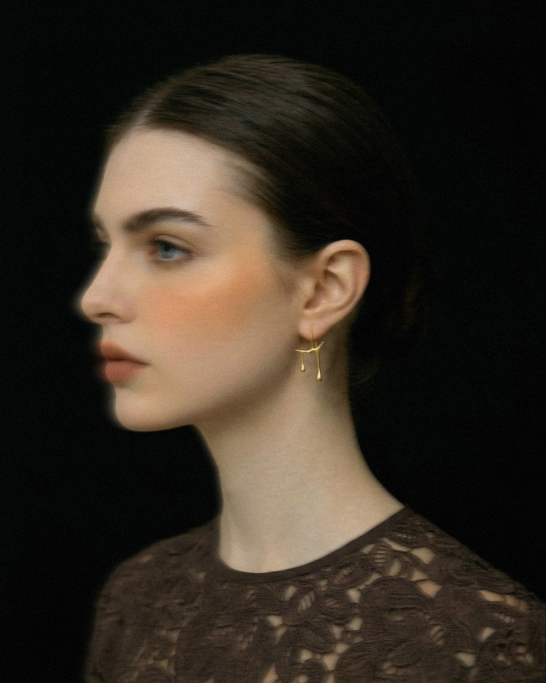 Woman wearing Chopin gold earring against a black background