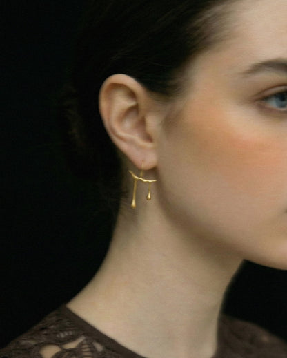 Close-up of a person wearing Chopin gold earrings with a blurred background