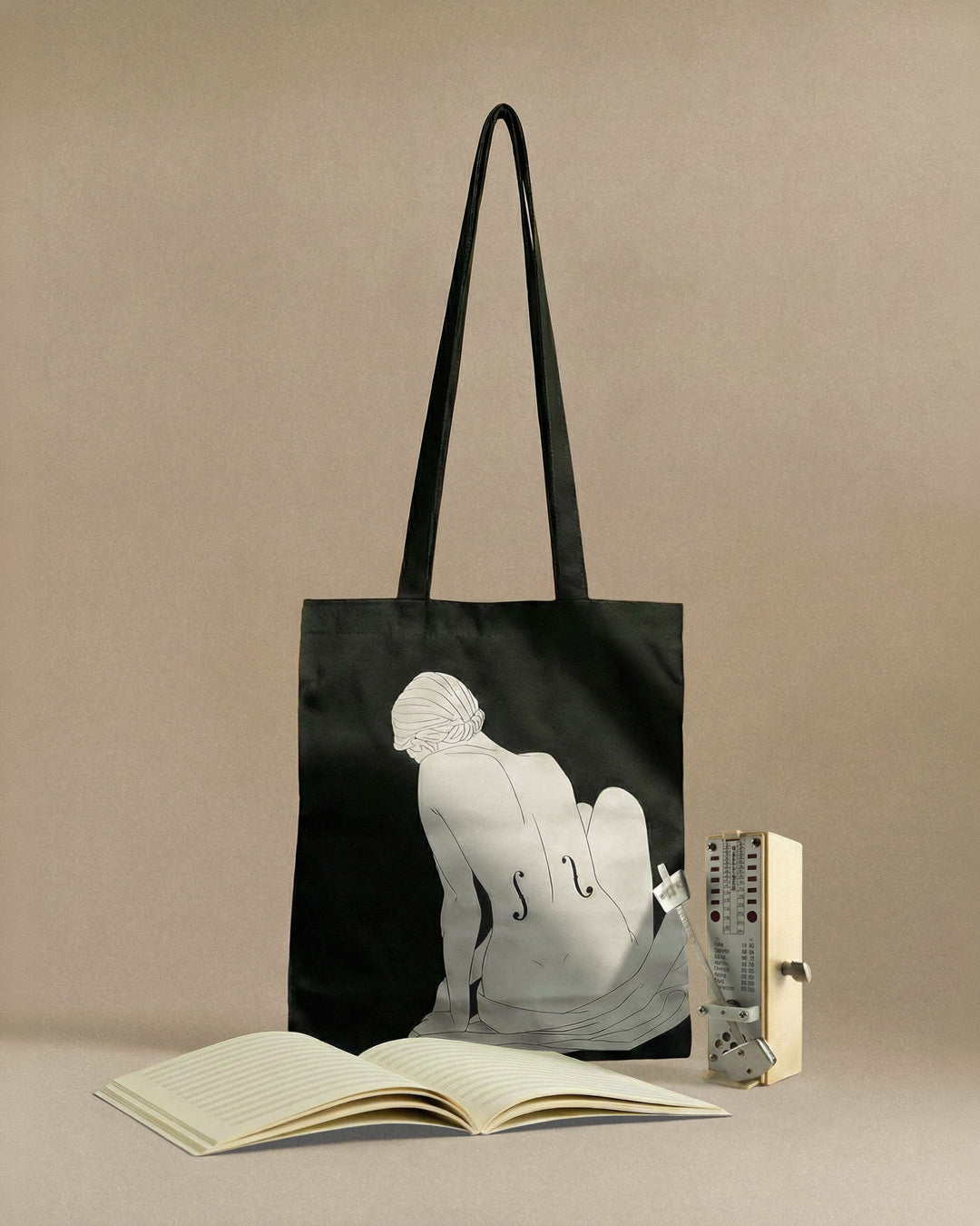 Black tote bag with artistic design of a person and a book on a beige background