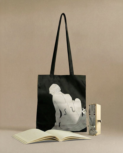 Black tote bag with artistic design of a person and a book on a beige background
